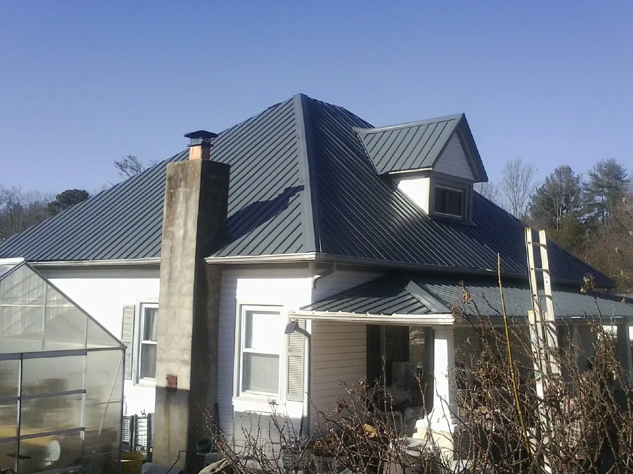 Dark blue standing seam metal roof on a white farmhouse with dormer — Slate & Tile Roof Repair by Roofing Brothers in Joint Base Mdl