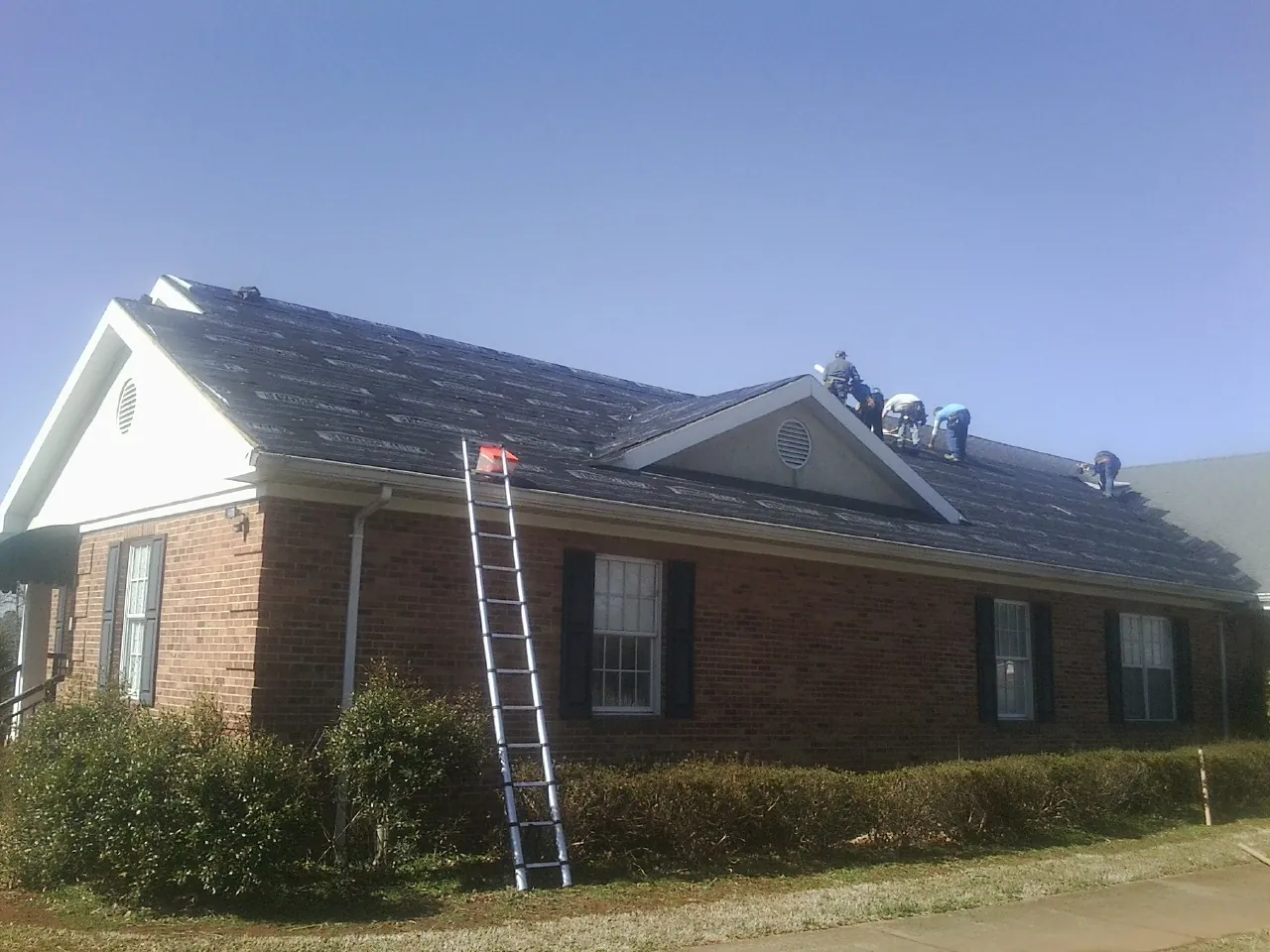 Crew tearing shingles off a brick ranch roof with a ladder set — Emergency Roof Repair work by our crew in Joint Base Mdl