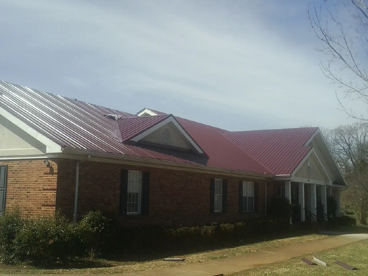 Red metal roof with gabled entries on a long brick building, from a Hail Damage Roof Repair job in Joint Base Mdl
