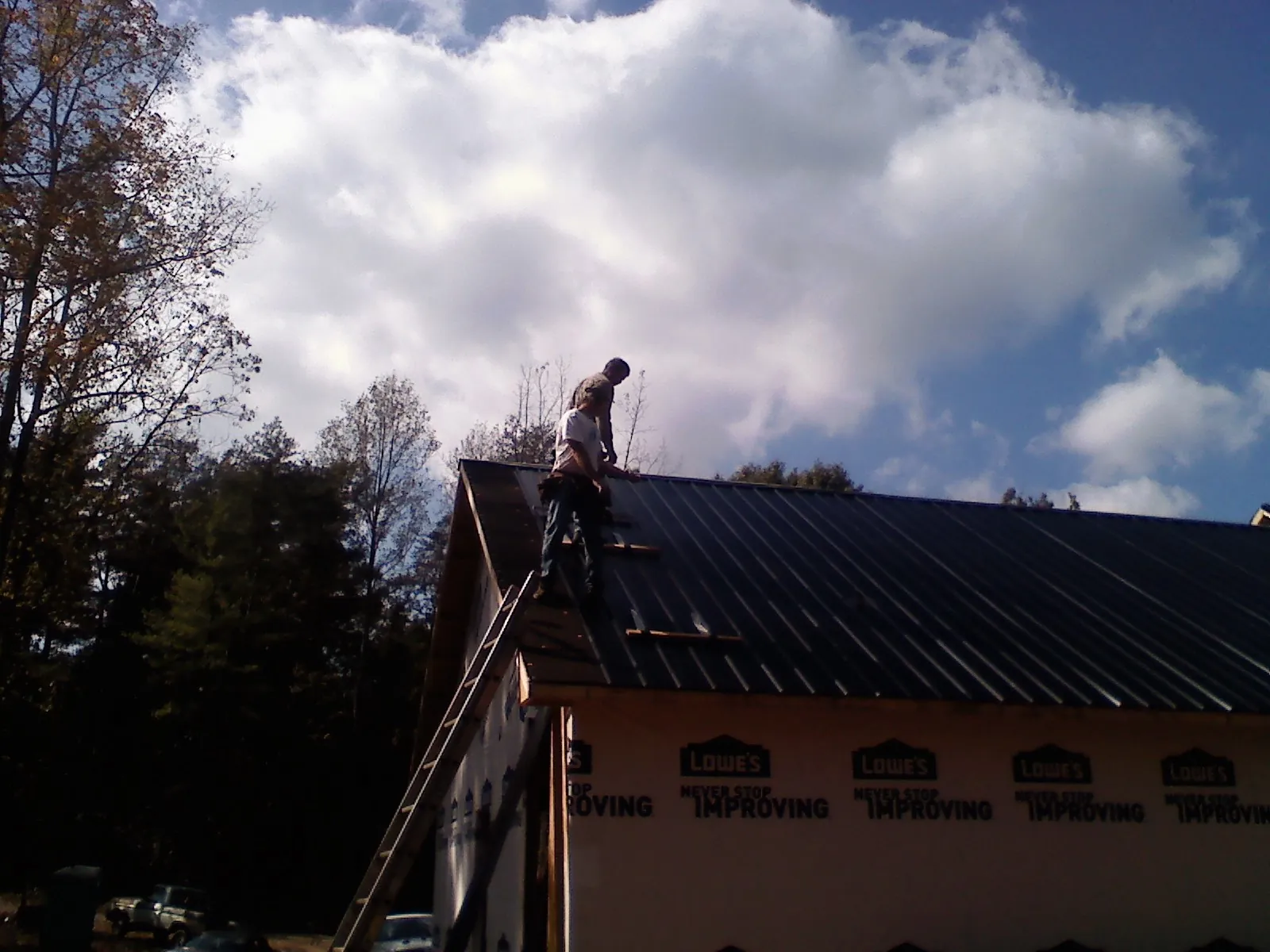 Roofer fastening dark metal panels high against a cloudy sky, from a Roof Inspection job in Joint Base Mdl