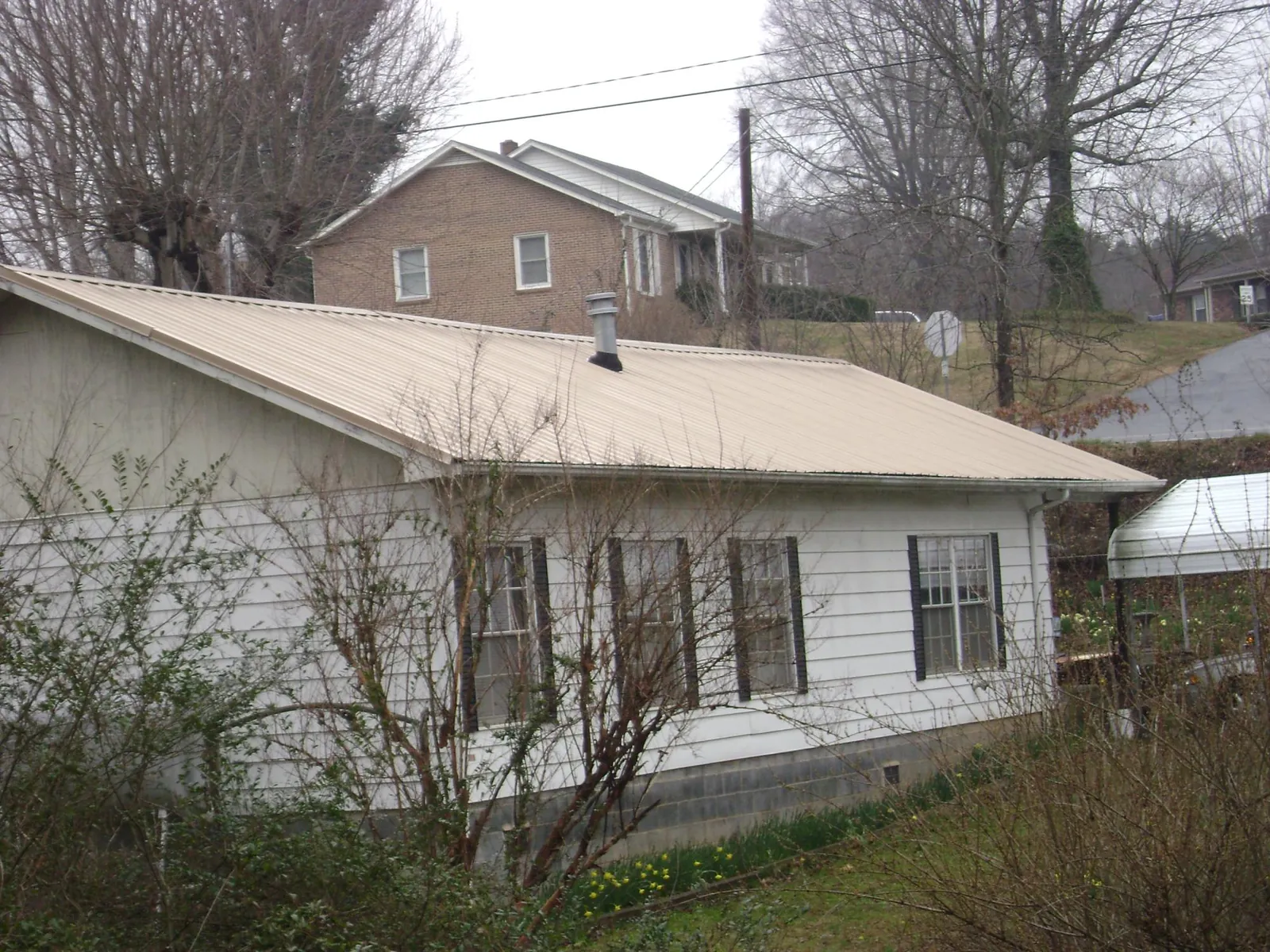 Tan metal roof on a white sided house set into a hillside — Commercial Roofing by Roofing Brothers in Joint Base Mdl